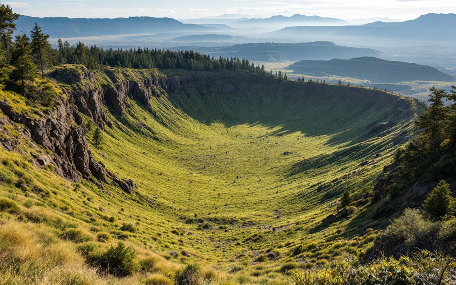 A broad grassed caldera floor seen from the forested rim across it, the far rim on the horizon