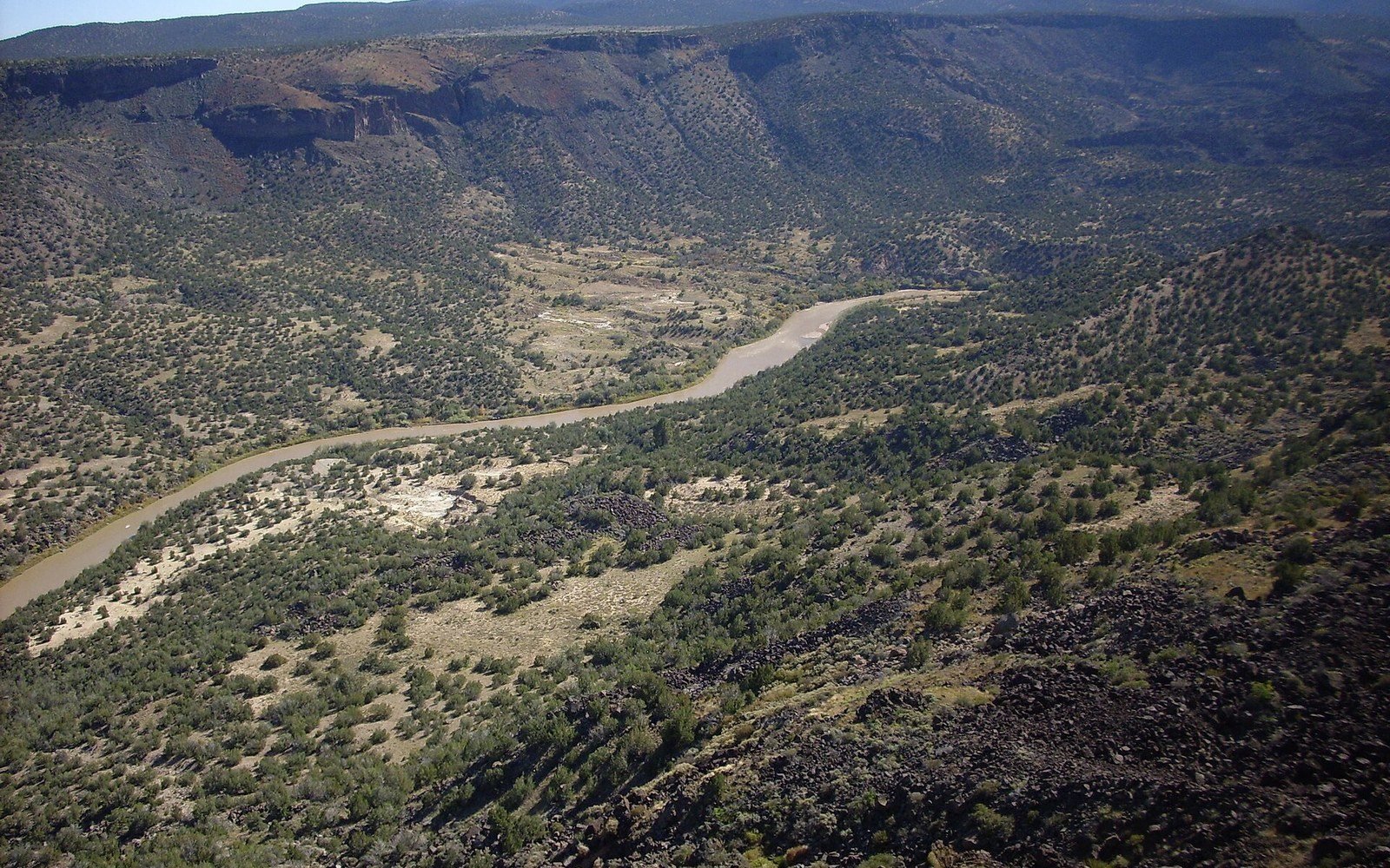 Aerial view of a winding river cutting through White Rock Canyon's shrub-covered slopes