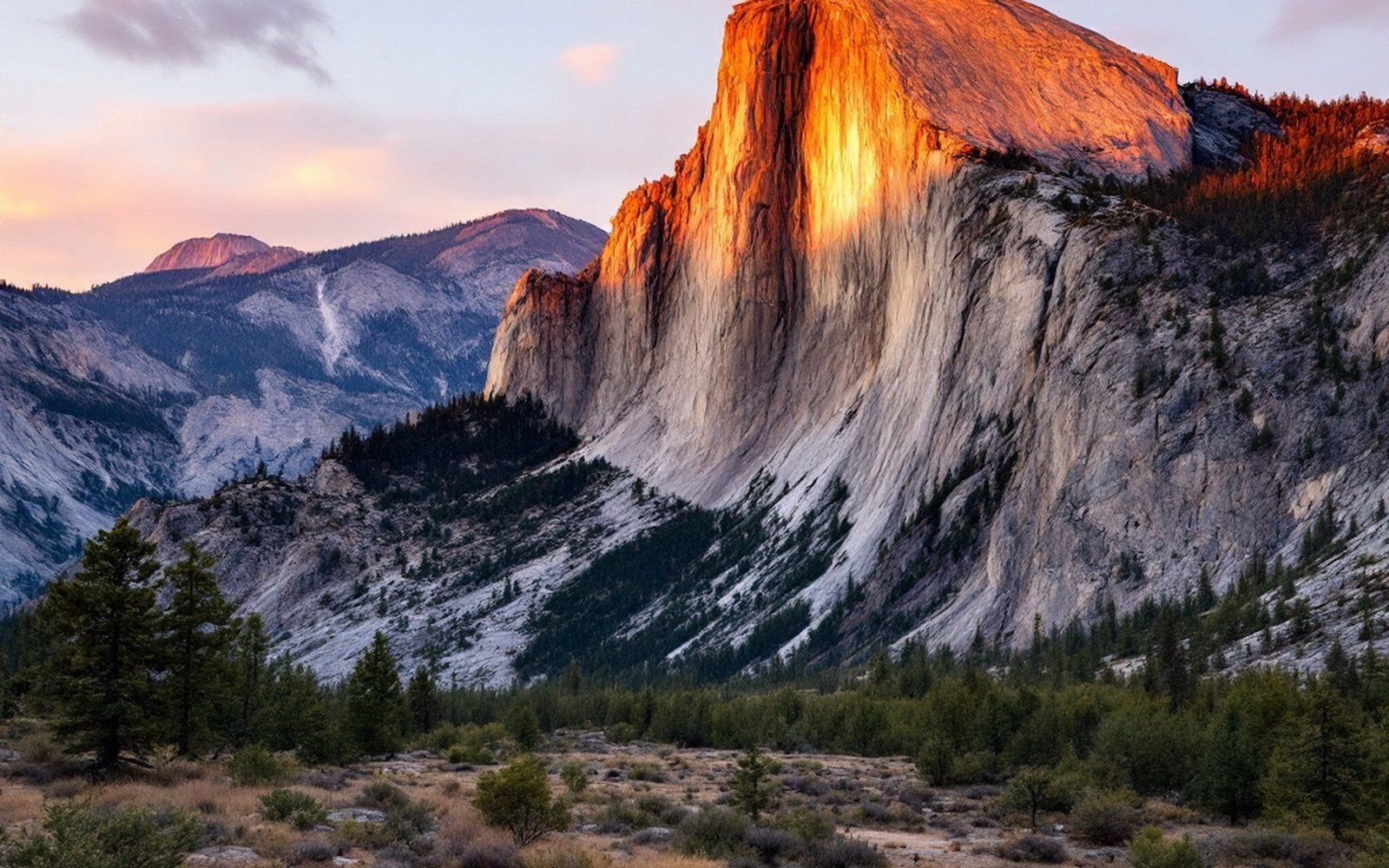 Sunset light glows orange on a granite cliff above a pine forest valley