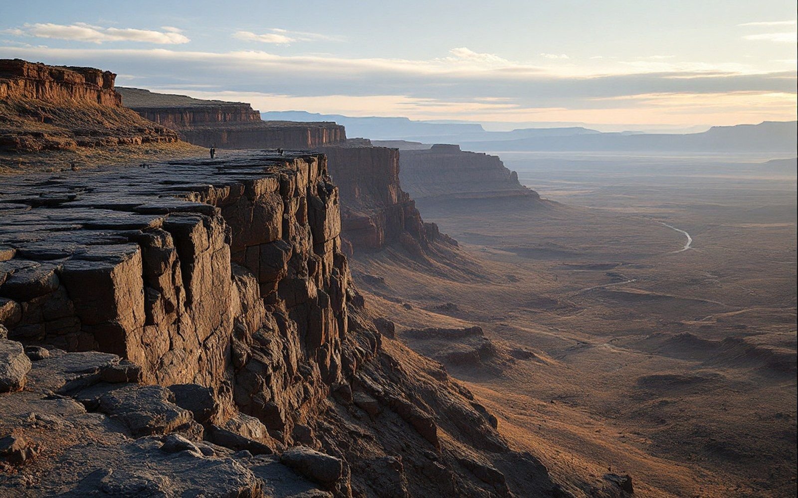 Rocky escarpment overlooks a vast desert valley under a hazy sky at dusk